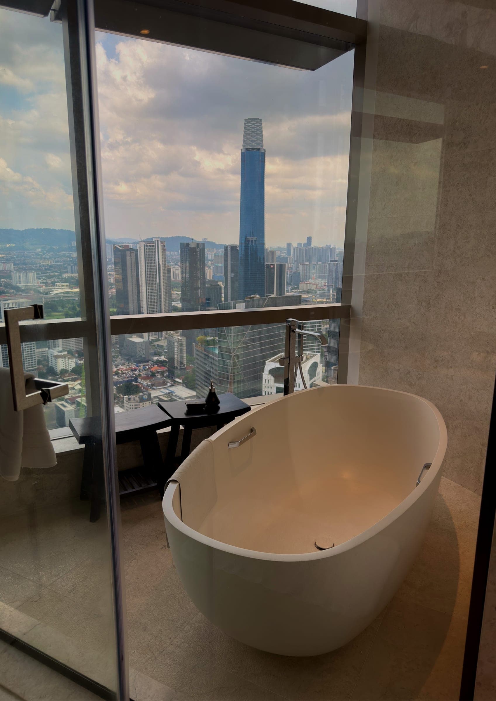 A freestanding bathtub beside a window looking onto the Merdeka 118 tower