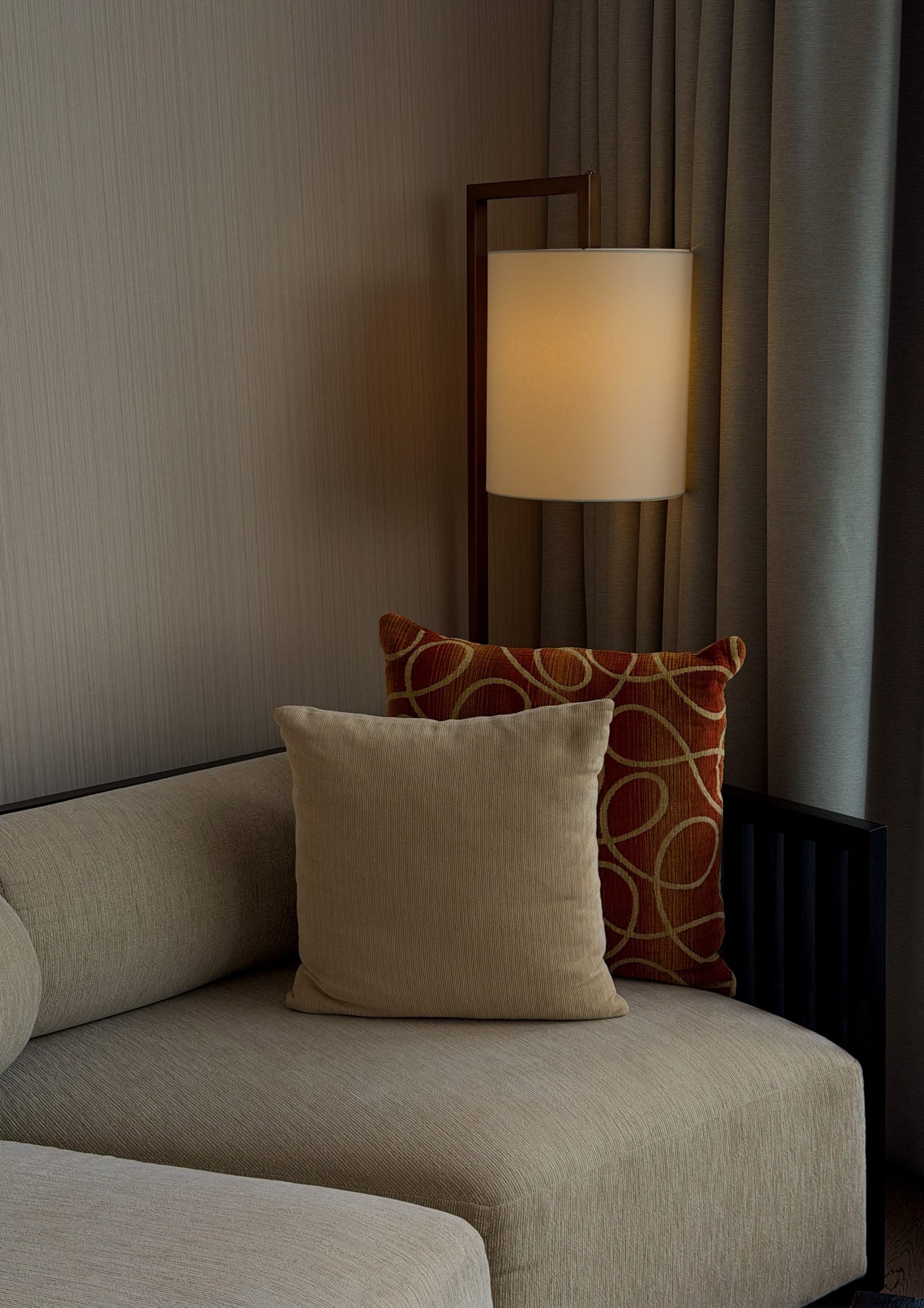 A cushion and slim floor lamp against textured wallpaper