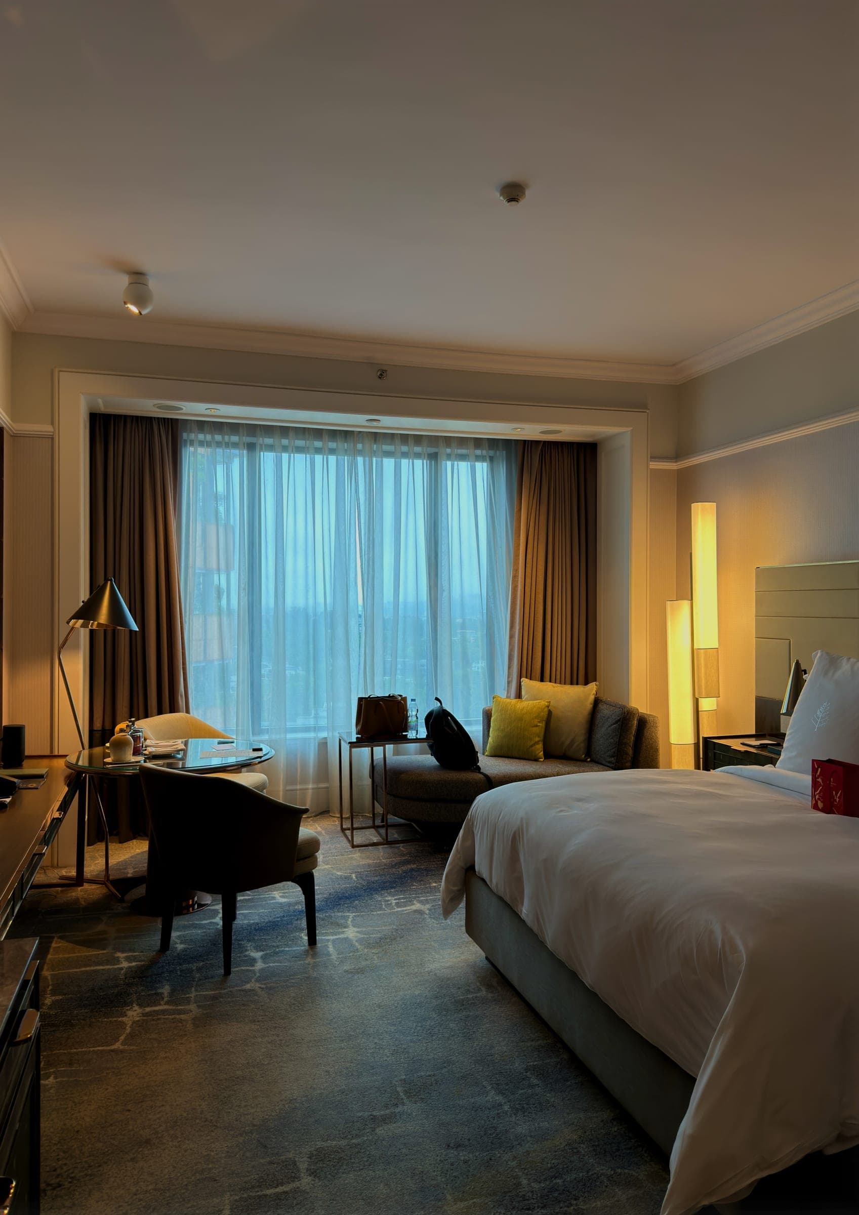 A warmly lit guest room with a bed, curtained window and reading corner