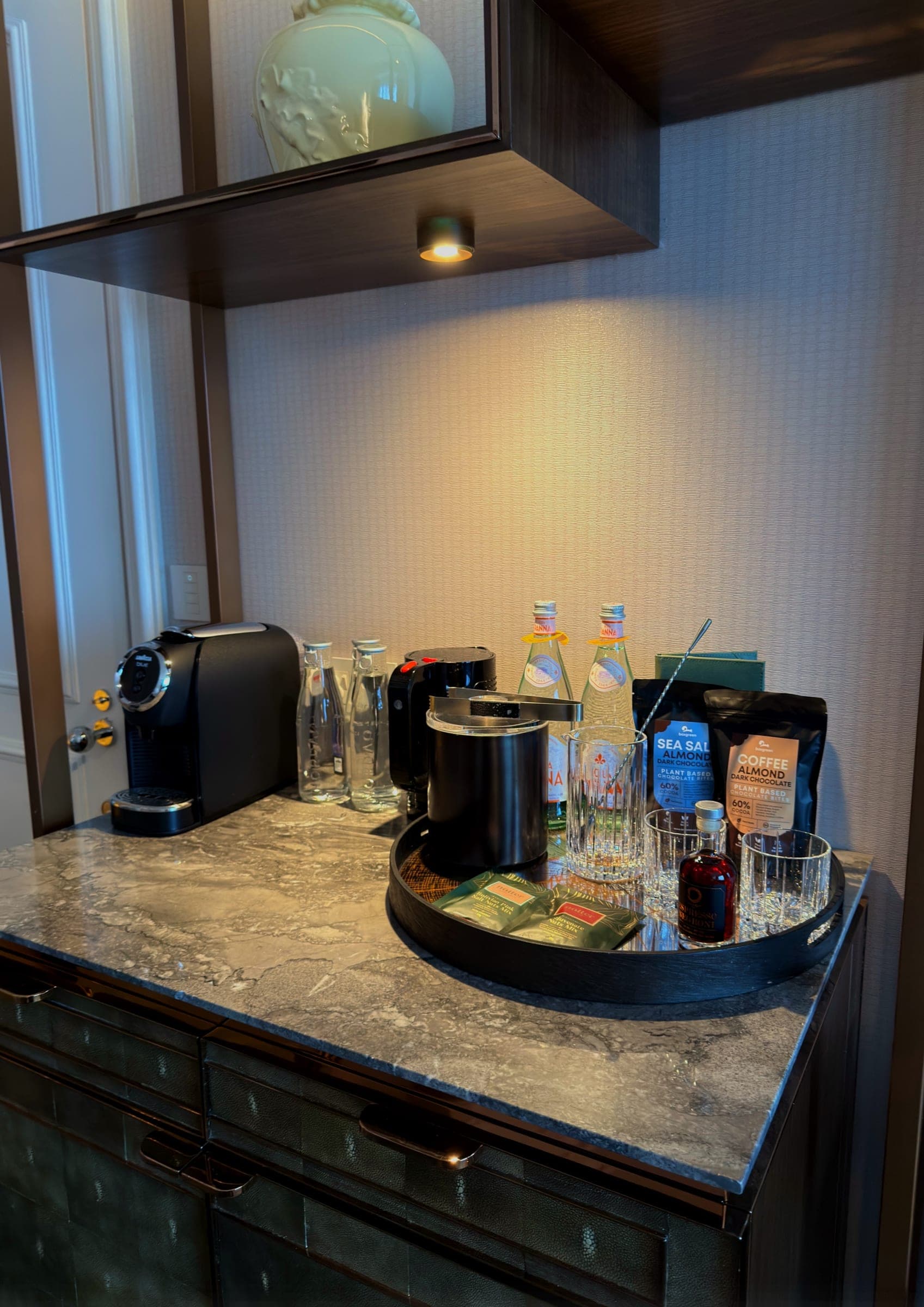A minibar tray with a coffee machine and water on a marble top