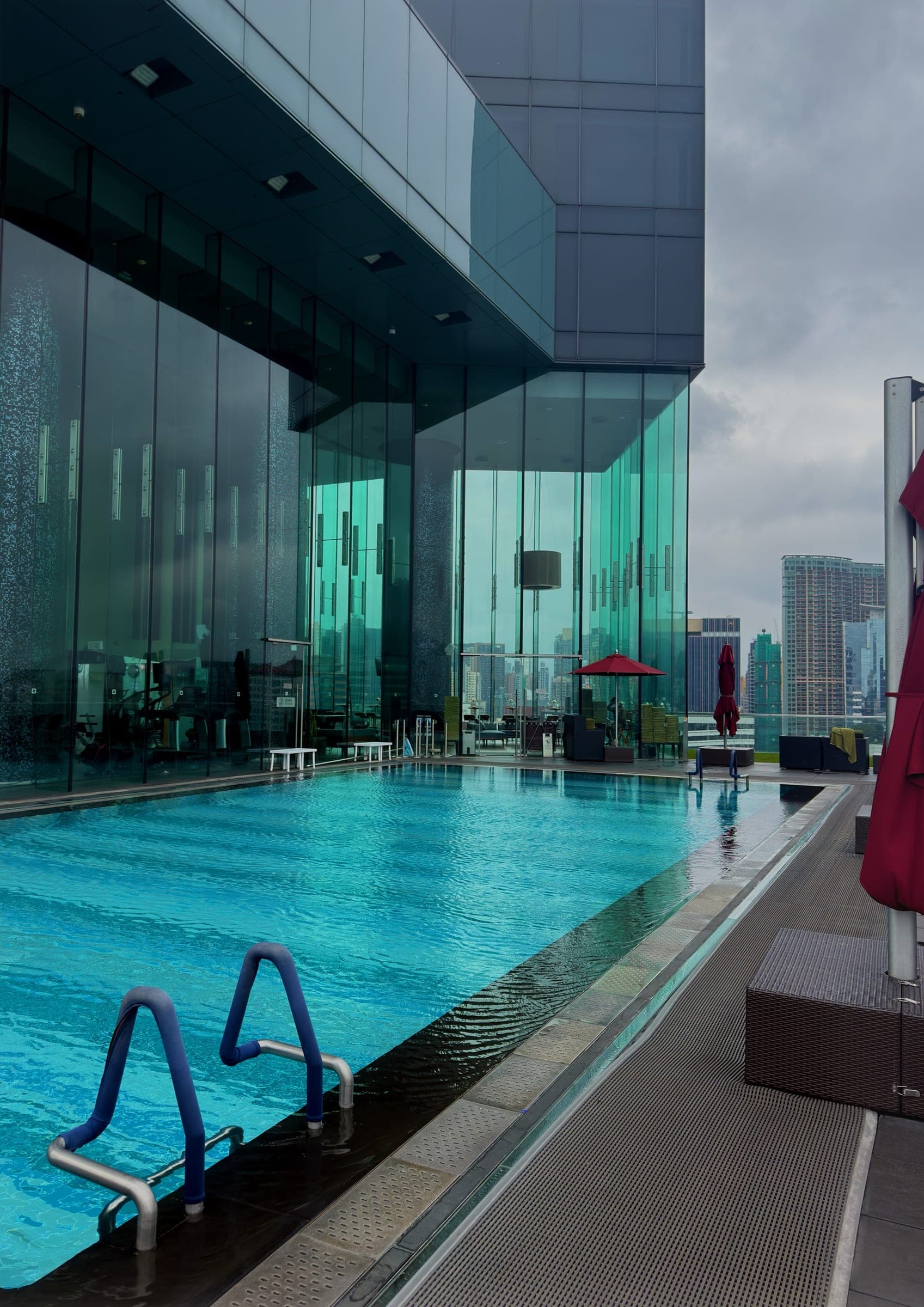 A rooftop pool set against a glass tower under grey sky
