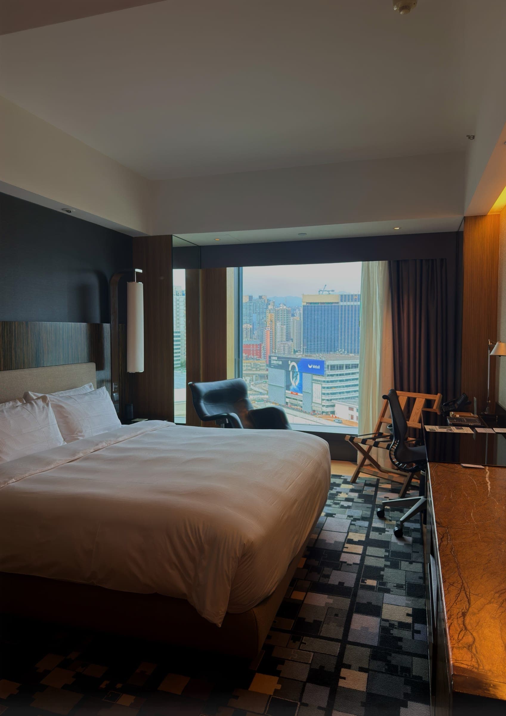 A guest room with a wide window looking over the Kowloon skyline