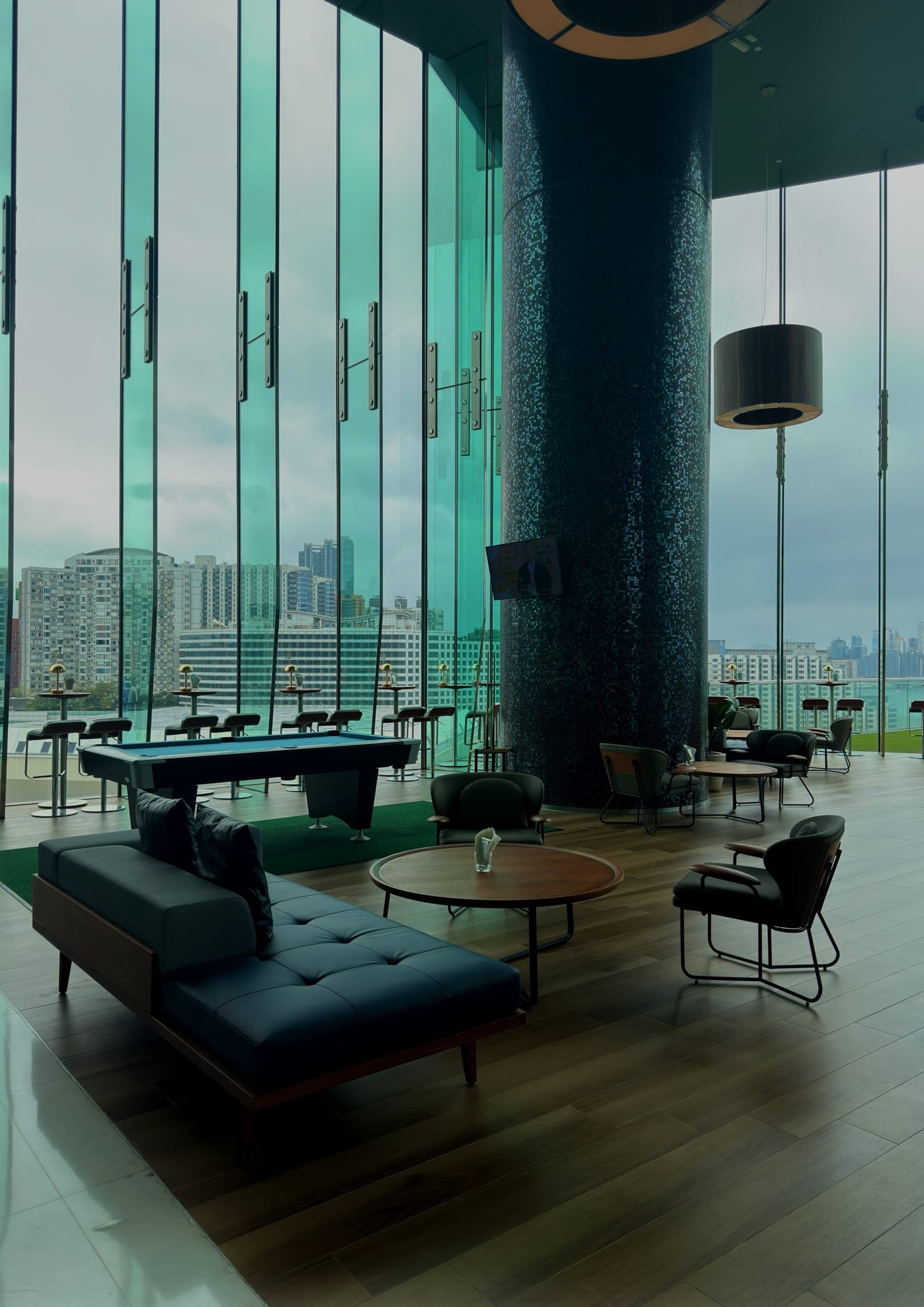 A double-height lounge with green glass walls and a mosaic column