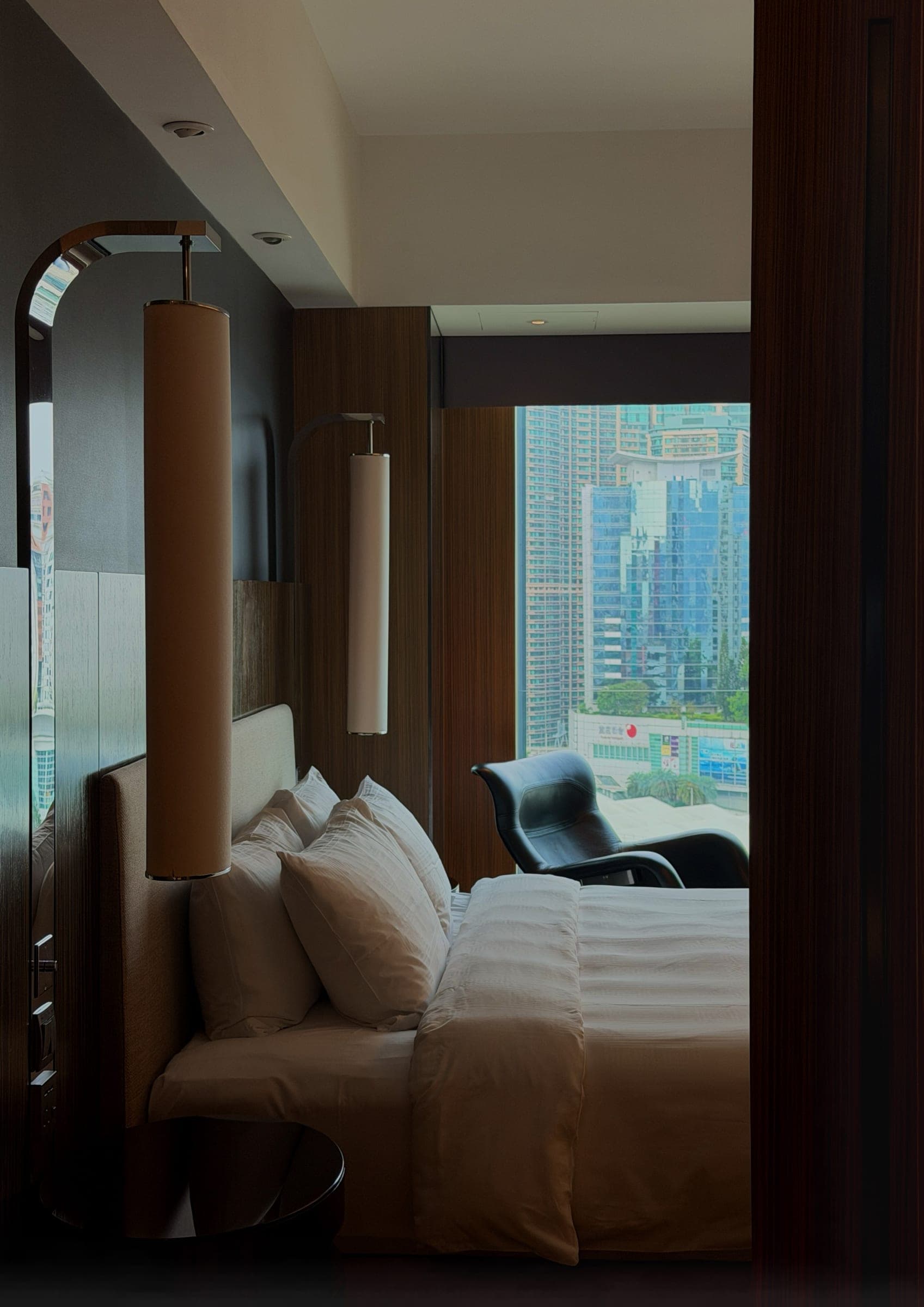 A bed with warm cylindrical lamps and a city view beyond