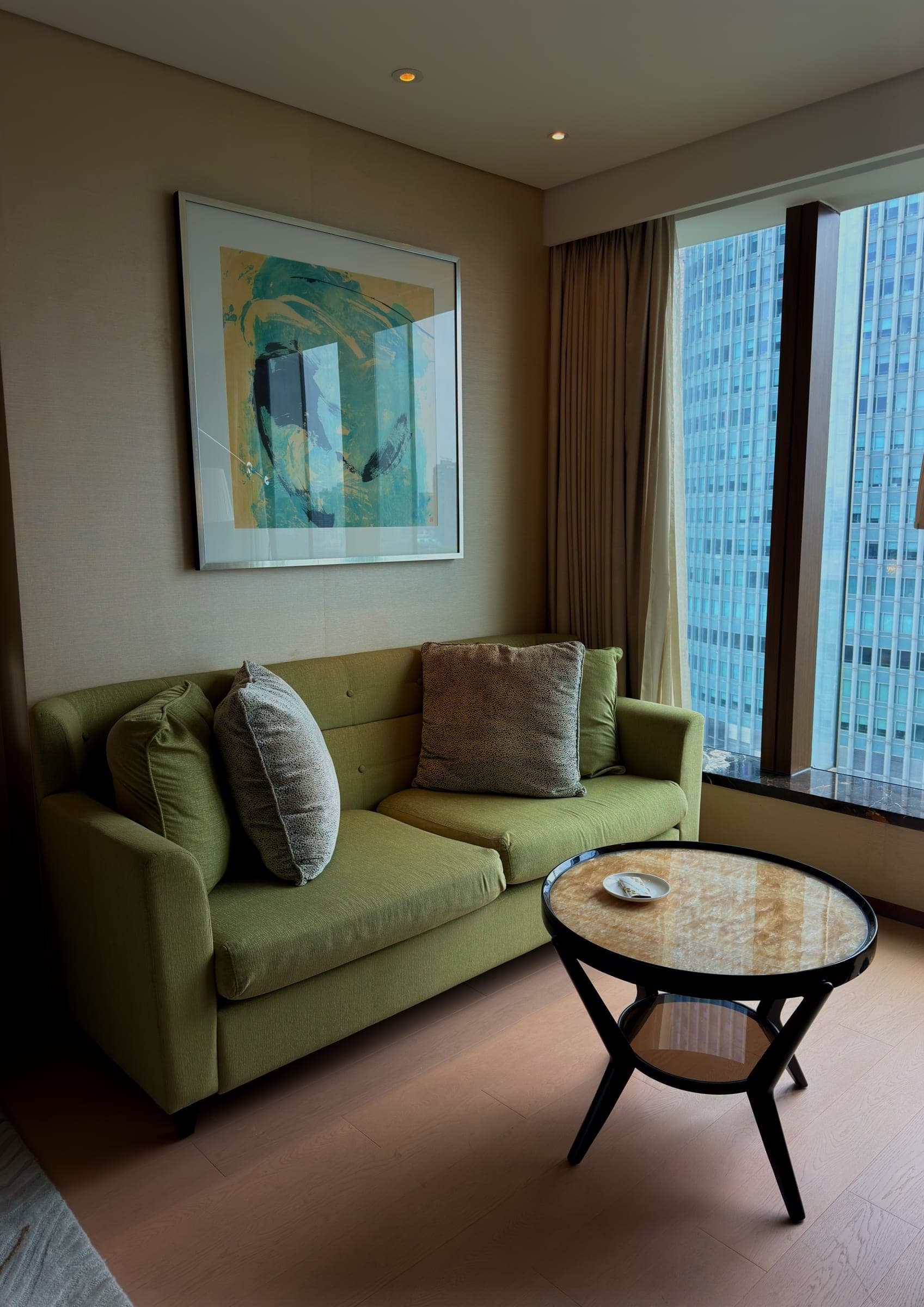 A green sofa beneath abstract art with a marble table by the window