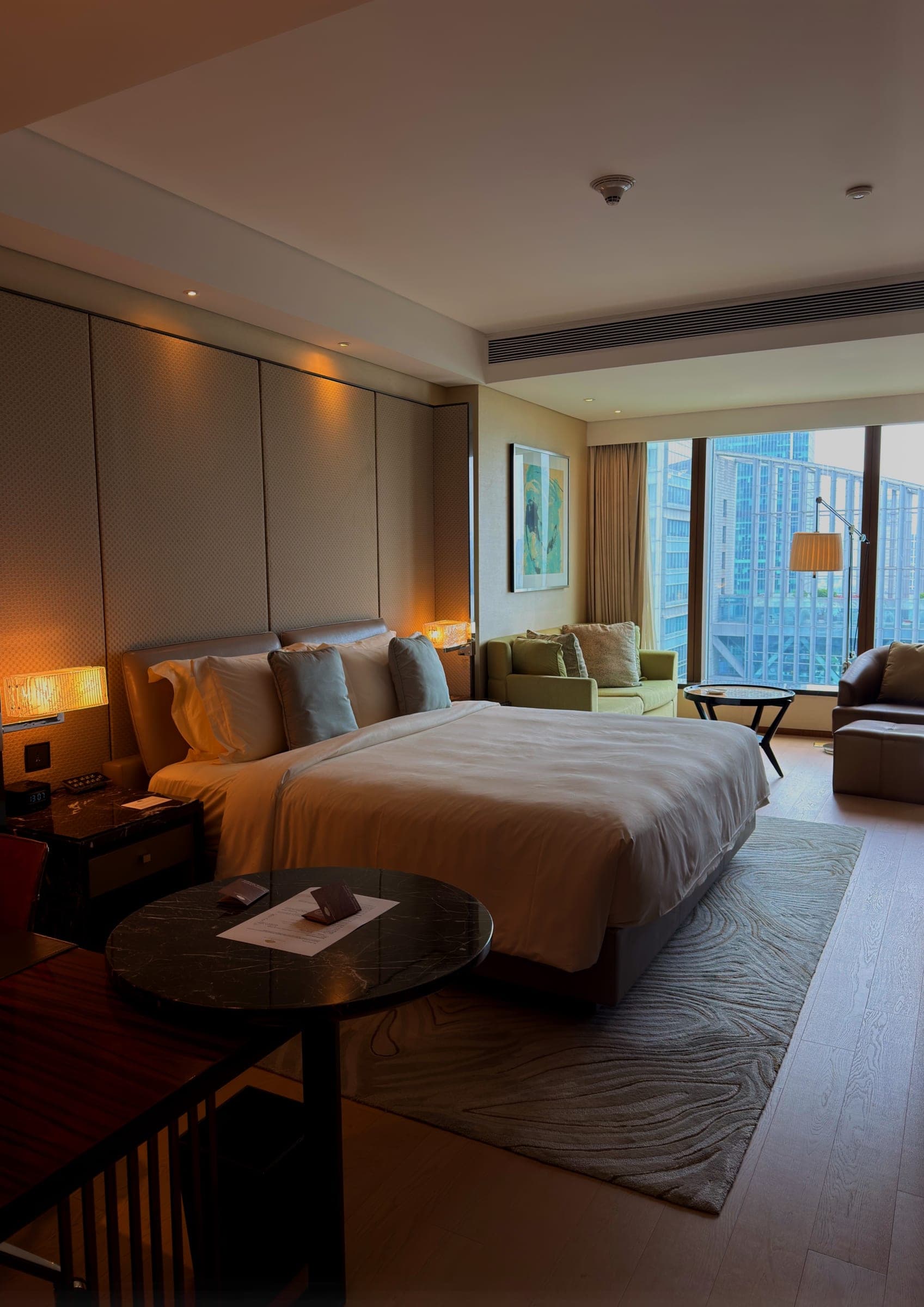 A guest room with a wide window, green armchair and warm lighting