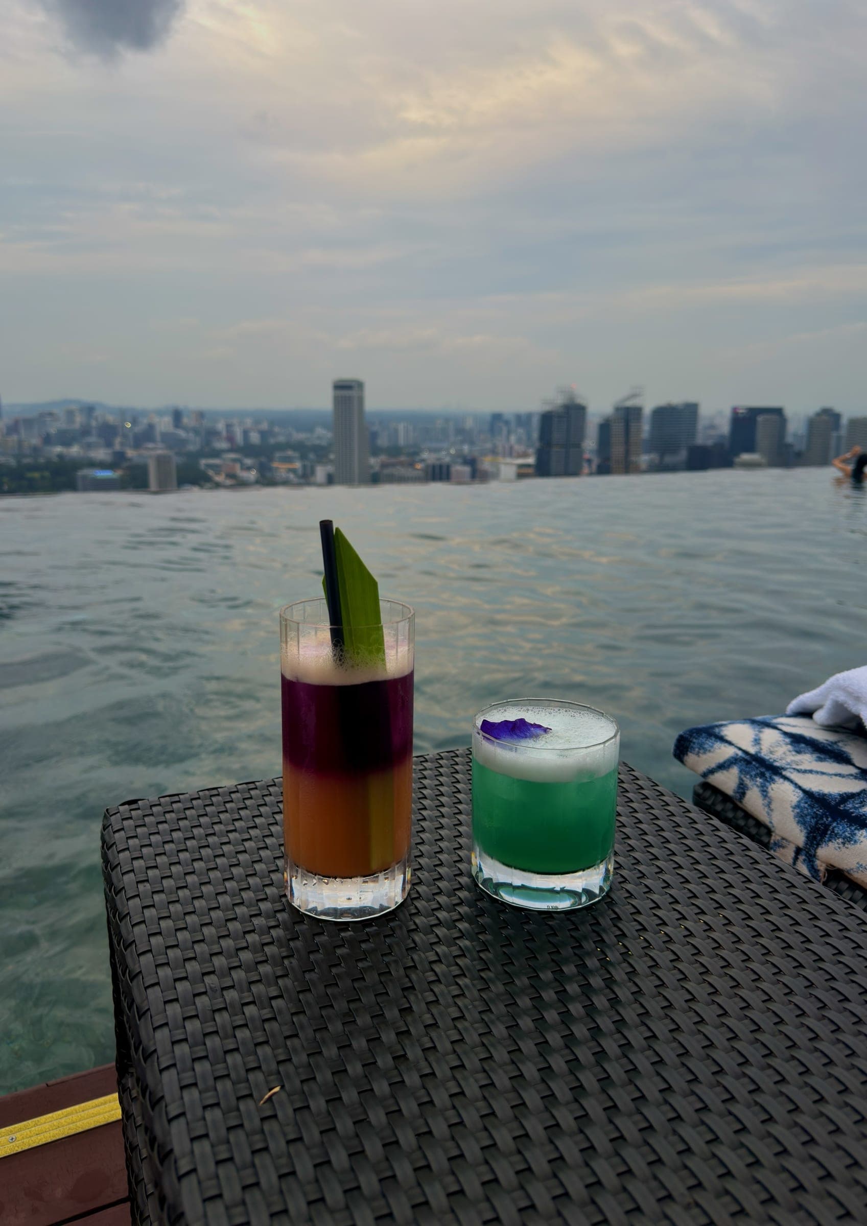 Two cocktails set on the pool edge above the skyline at dusk