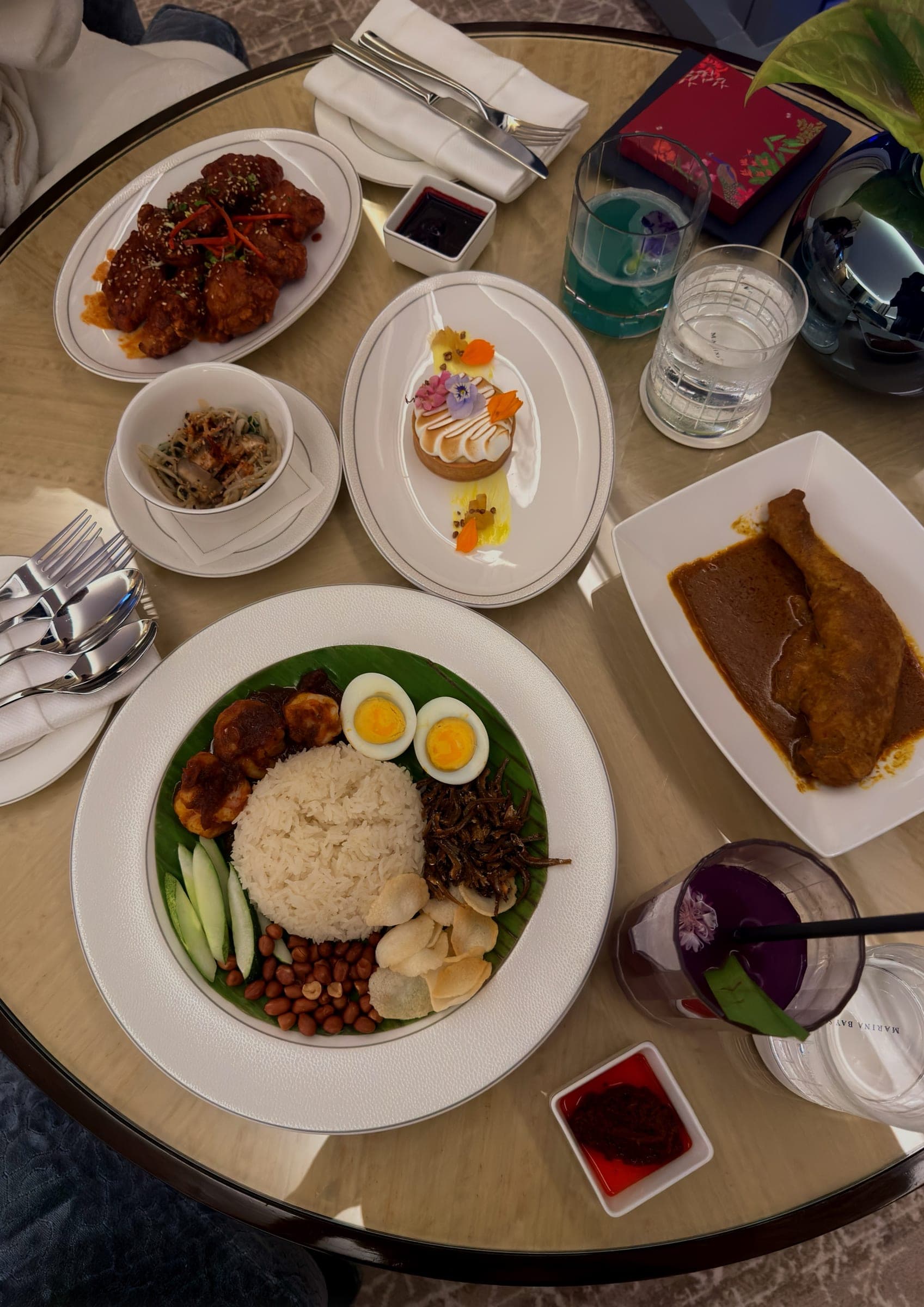 An in-room dining spread with nasi lemak, curries and cocktails