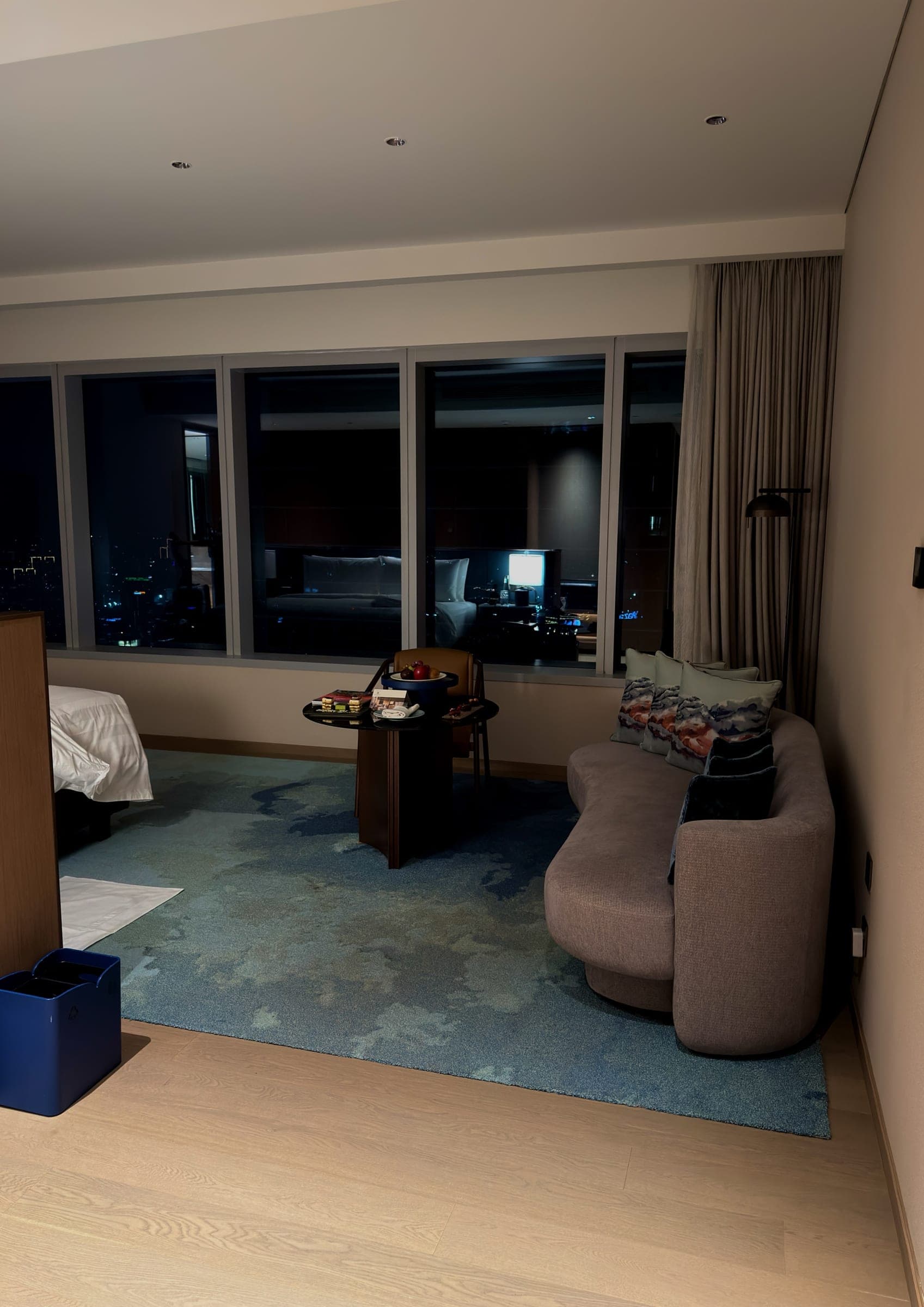 A curved sofa in a suite living area with the city lit beyond the glass