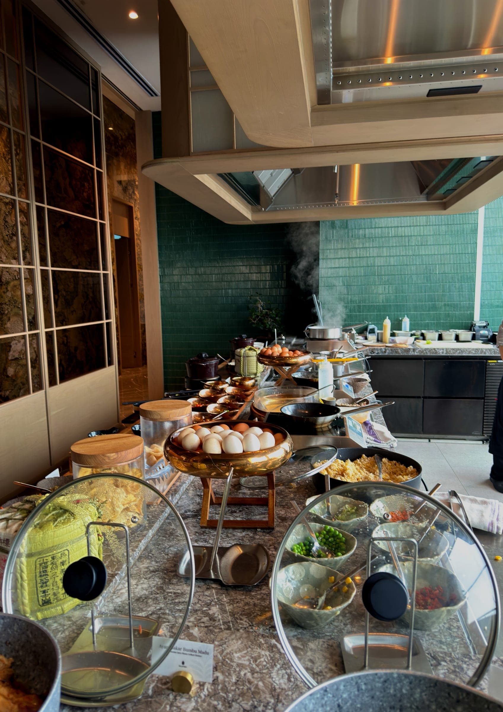 A breakfast buffet with a live cooking station and green tiled wall