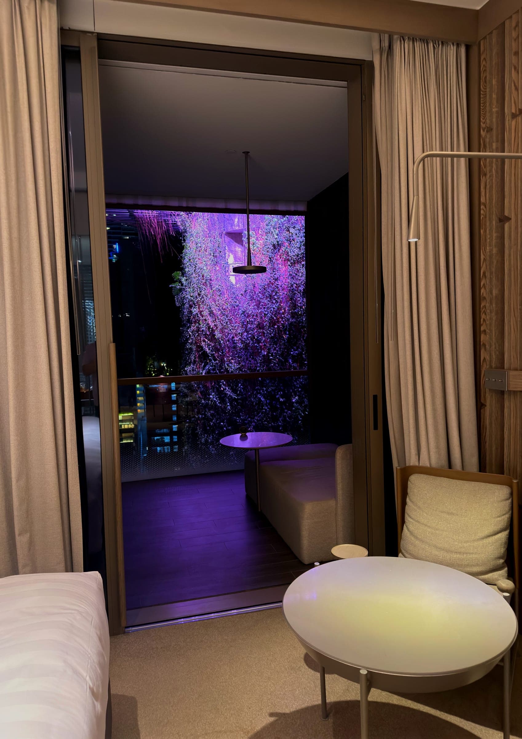 A room opening onto a balcony above an illuminated planted terrace
