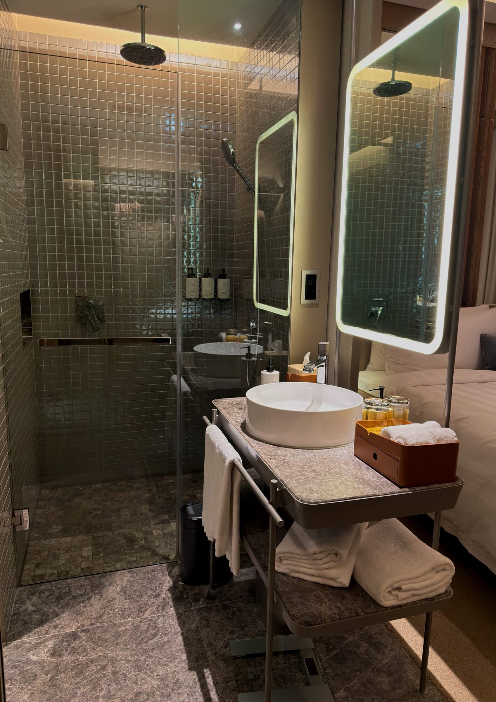 An open bathroom with a walk-in rain shower beside the bed