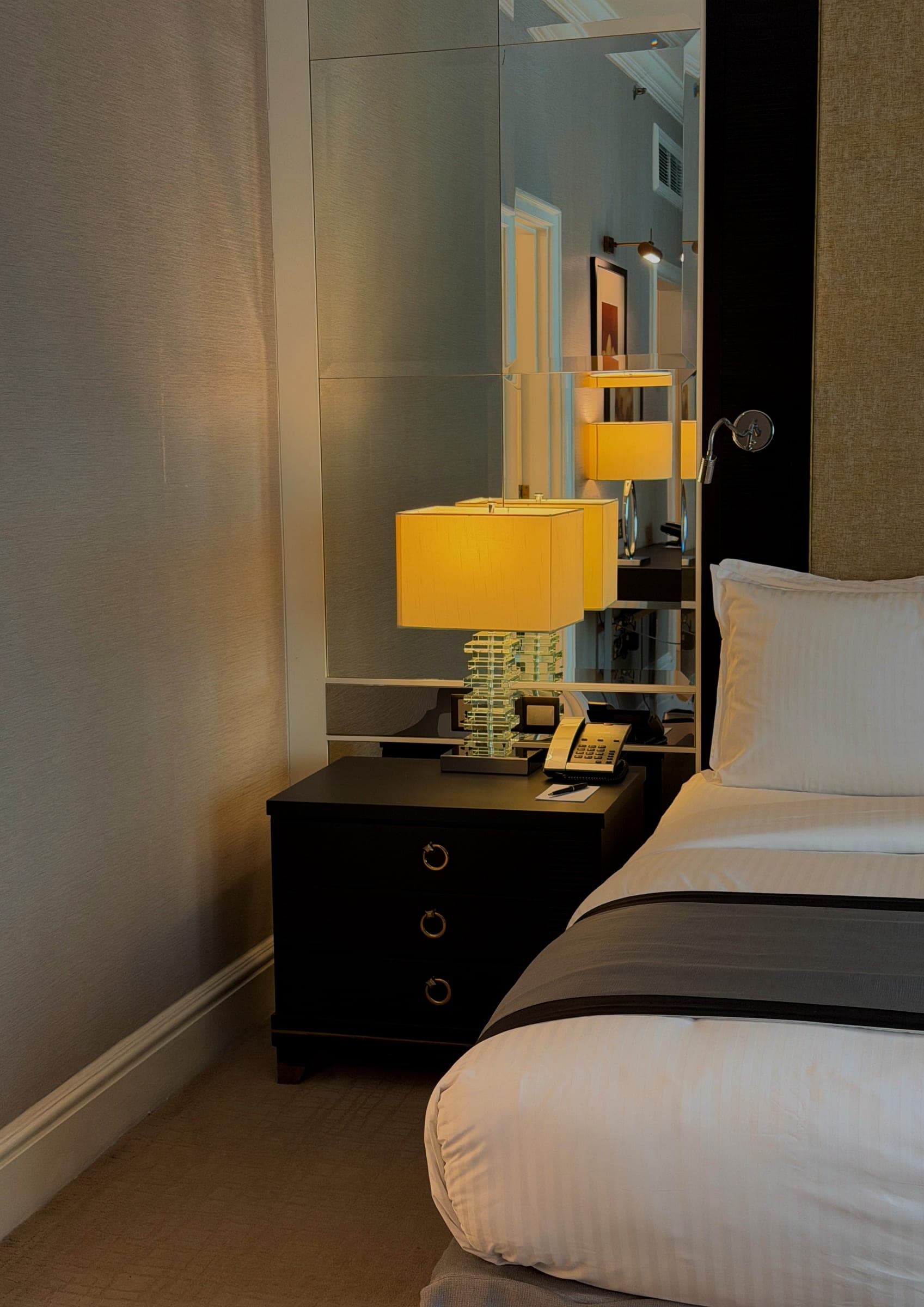 A bedside table and lamp against a mirrored panel
