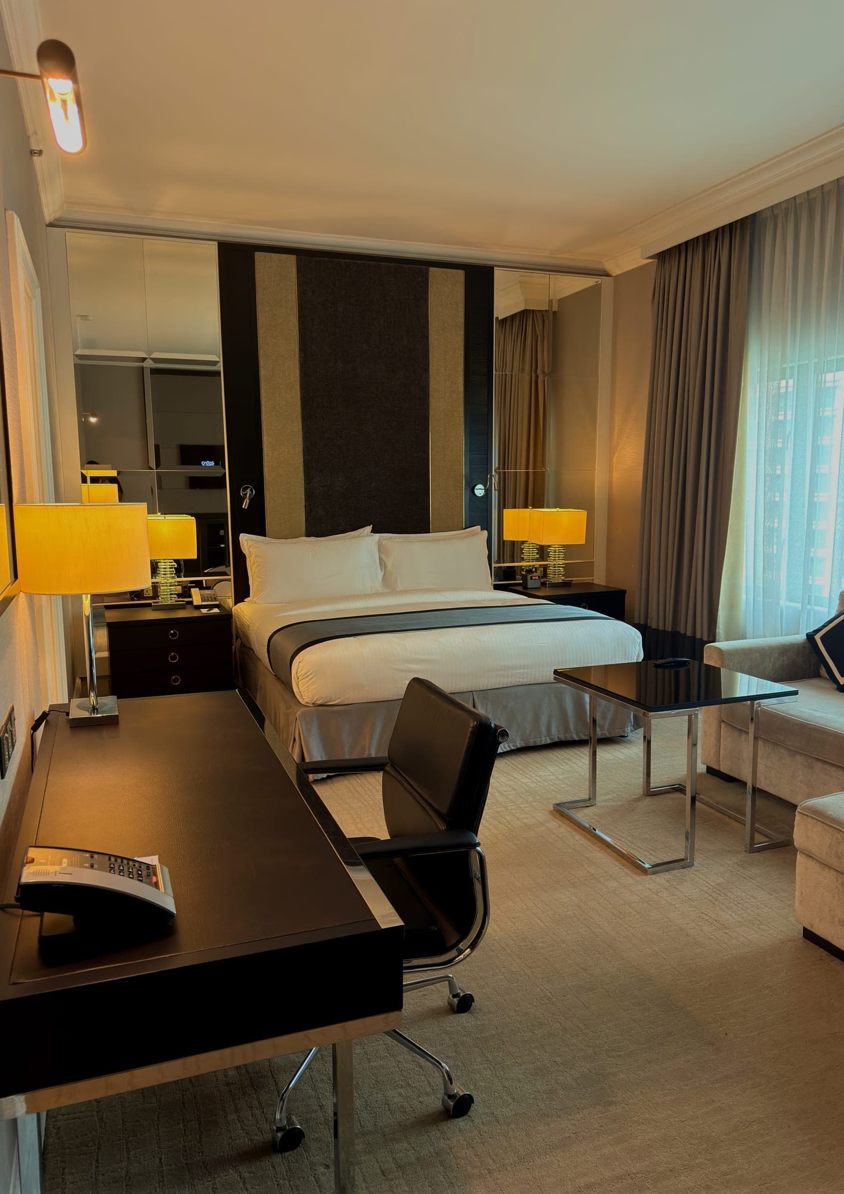 A classically furnished guest room with dark timber and a city window