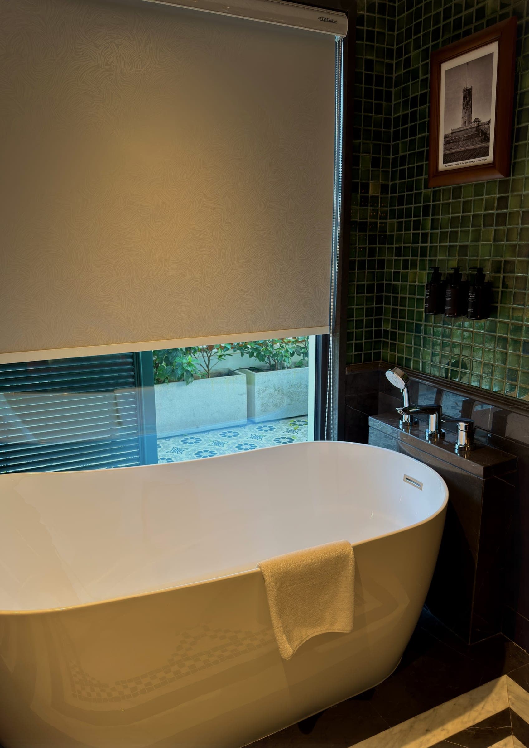 A freestanding bathtub beside a window looking onto a tiled courtyard