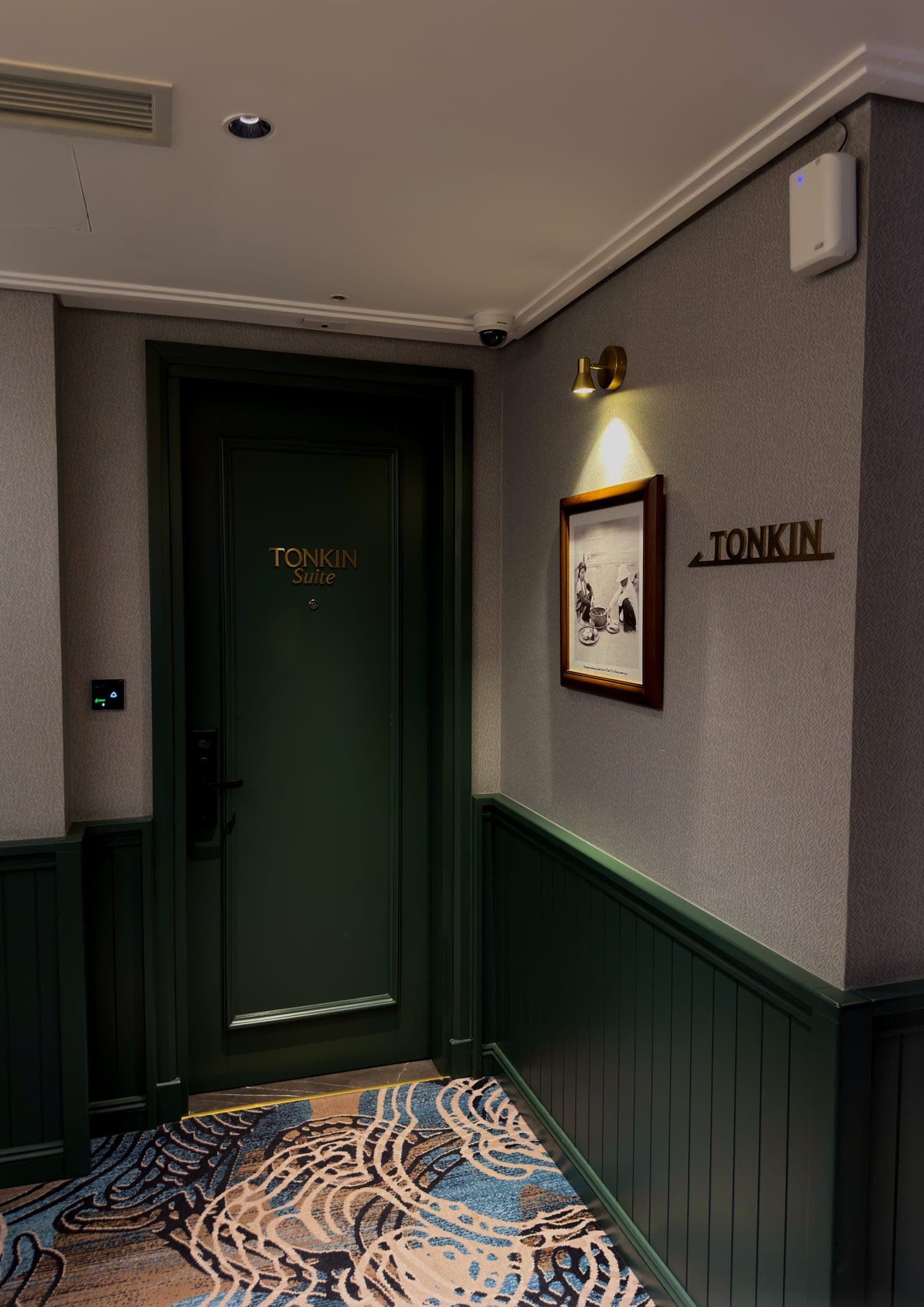A corridor with a green Tonkin Suite door, wainscoting and a patterned carpet