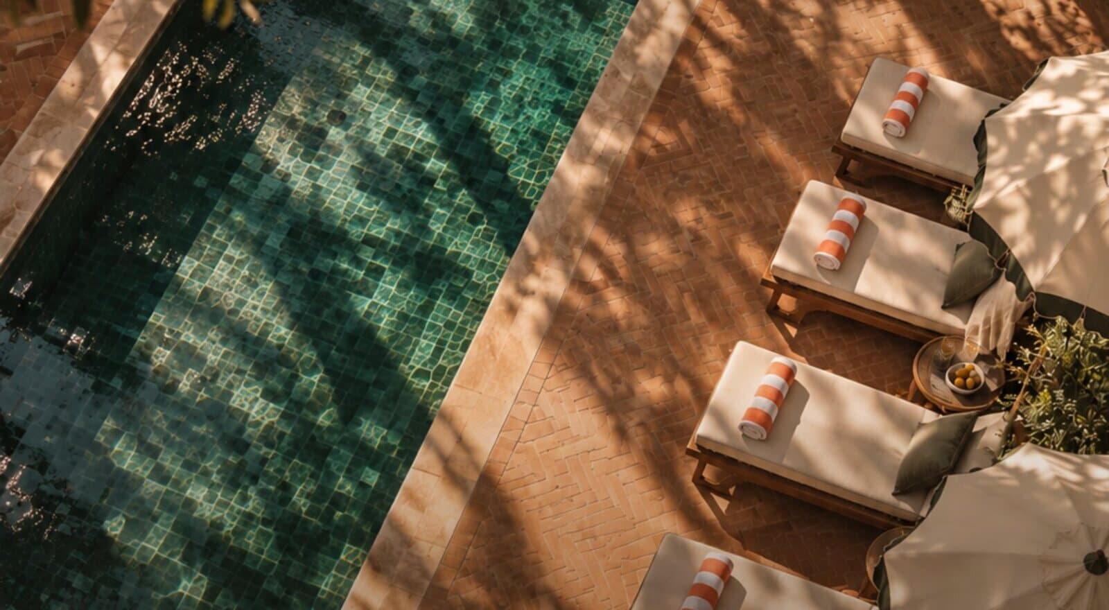 A painted view over a green tiled pool and a row of sunlit loungers
